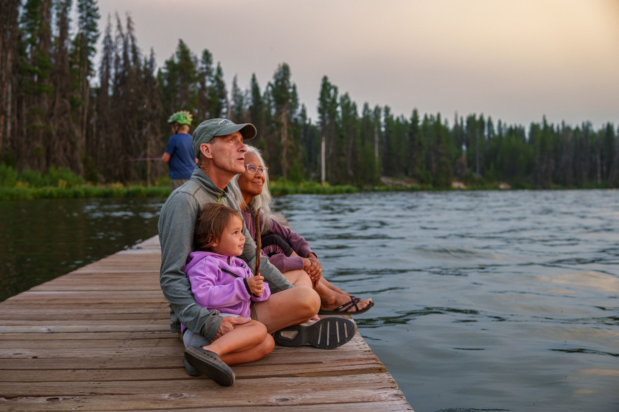 Grandparents and granddaughter enjoy sunset on a lake dock