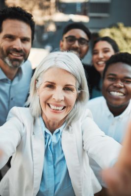 Shot of a mature businesswoman standing outside with her colleagues and taking selfies