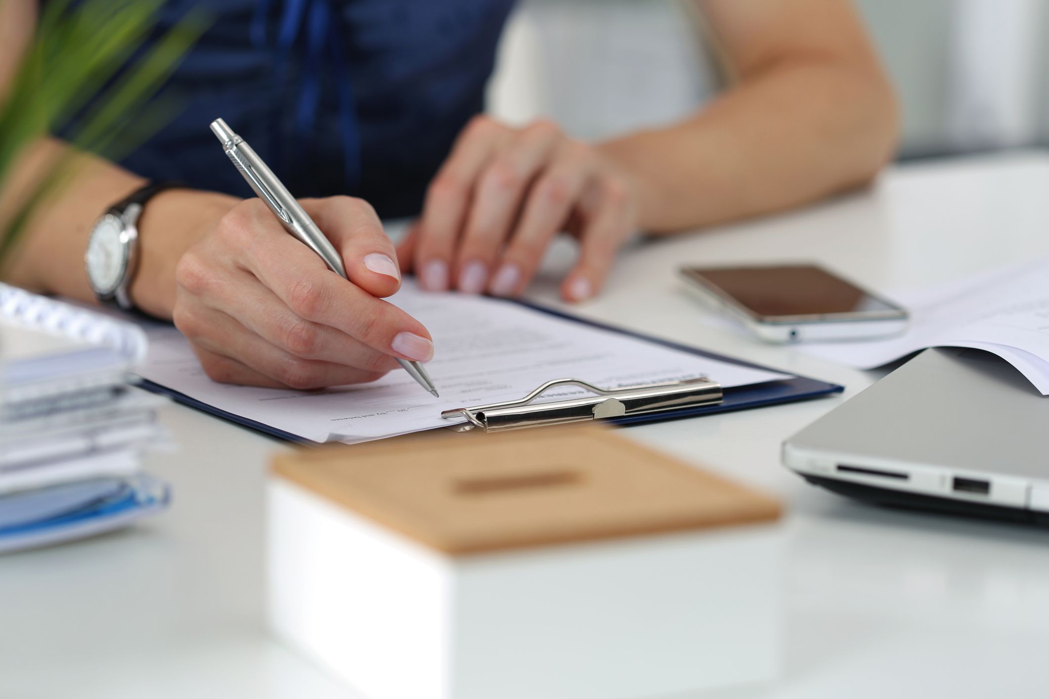 Woman writing something and looking at mobile phone screen sitting at her office